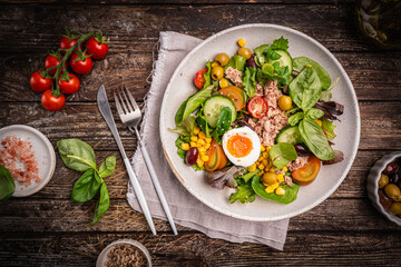 Tuna salad with tomatoes, cucumber, corn, olives , eggs and onion on wooden background, top view. High quality photo