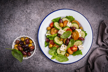 Greek salad of fresh cucumber, tomato, sweet pepper, lettuce, feta cheese and olives with olive oil on a gray background. Healthy food, top view. High quality photo
