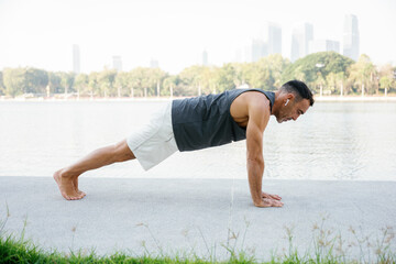 Mature man doing plank exercise by the lake in city park