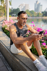middle aged athlete using smartphone and earbuds in urban park