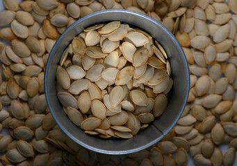 Fresh pumpkin seeds collected in a metal container surrounded by scattered seeds on a wooden surface