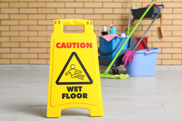 Janitor's trolley with cleaning supplies, caution sign and floor mop near brick wall