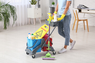 Janitor with trolley, floor mop and caution sign in office