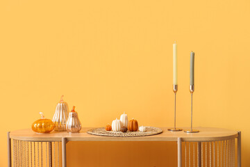 Shelving unit with candles in shape of pumpkin and decorations near yellow wall