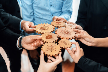 A group of diverse professionals shows collaboration by holding wooden gears representing security and innovation, symbolizing teamwork and strategic planning in business. Amity