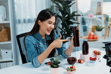 Smiling young beautiful Asian reviewing tasty mixed strawberry and cherry juice detox drinks,...