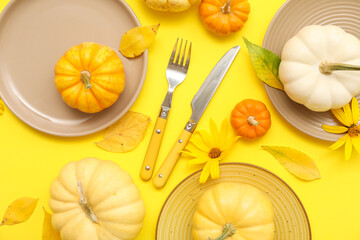 Beautiful table setting with fresh pumpkins, flowers and autumn leaves on yellow background