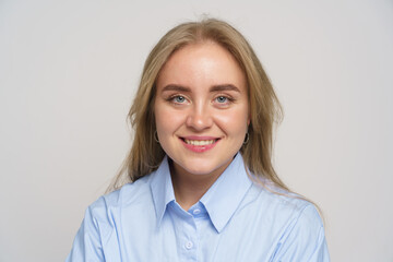 Young woman with blonde hair smiles confidently in a light blue shirt against a neutral background