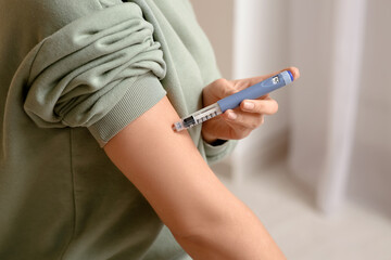Obraz premium Young woman with diabetes giving herself insulin injection at home, closeup