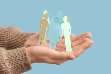 Female hands holding paper human figures on blue background