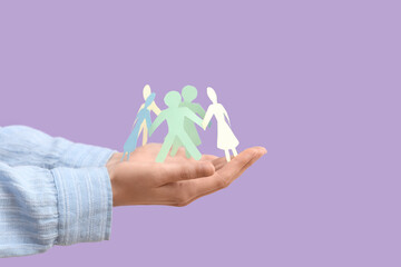 Female hands holding paper human figures on lilac background