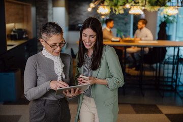 Two Women Collaborating in a Modern Workspace With Colleagues in Background