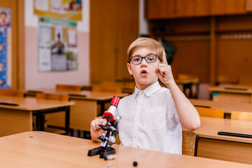 8-year-old smart schoolboy in glasses studying through a microscope at school