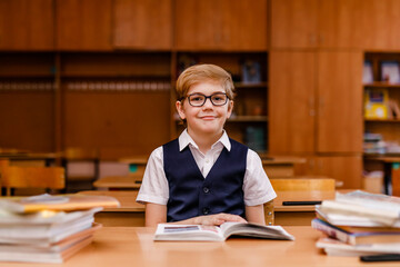 8-year-old schoolboy in glasses, white shirt, and vest studying and reading books in the classroom