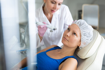 Adult woman getting oxygen face therapy in beauty salon. Professional skin care treatment, atomized...