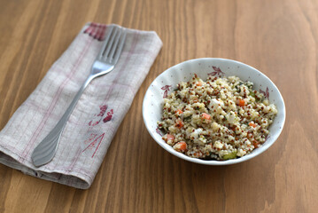 Quinoa salad in a bowl with fork on wooden background