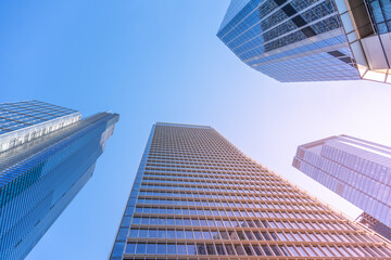 Fototapeta premium Tall glass skyscrapers dominate the skyline of the City of London, showcasing modern architecture under a clear blue sky during daylight hours. The buildings reflect a vibrant urban atmosphere.