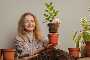 A woman smiling while potting a young plant in a terracotta pot, surrounded by soil and gardening...