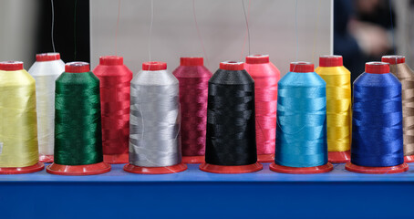 A row of colorful spools of thread are displayed on a table. The spools are of various colors and sizes, and they are arranged in a neat row. Concept of organization and attention to detail