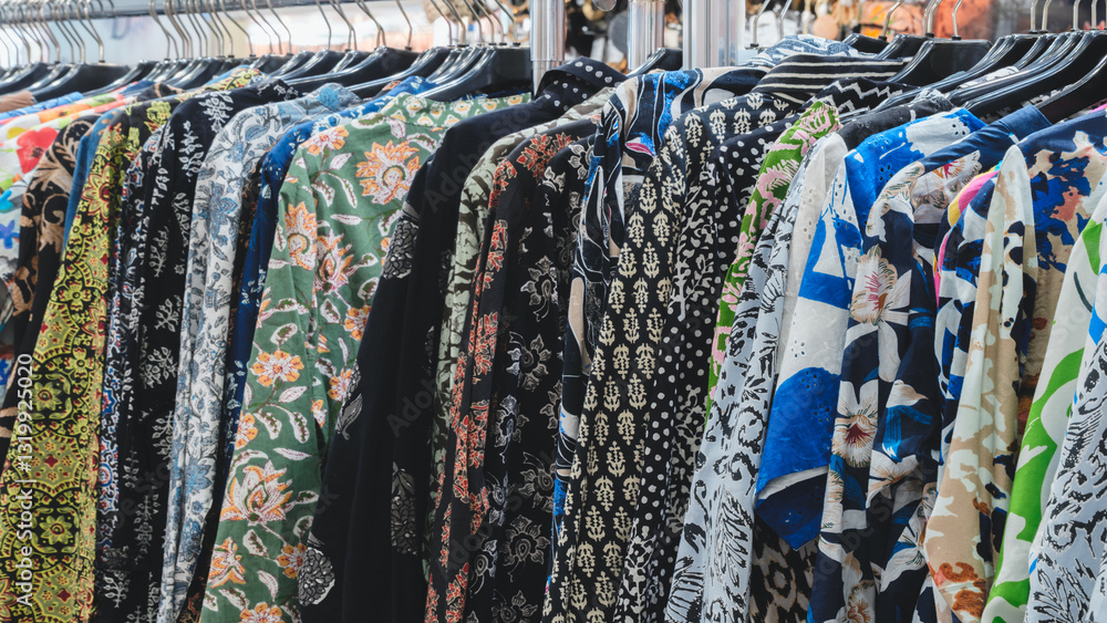 Poster a rack of clothes with a variety of patterns and colors. the clothes are hanging on hangers and are 
