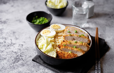 Ramen noodles with meat schnitzel slices, peking cabbage, eggs and scallions in a bowl