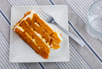 Sweet and fragrant dessert, pastries for tea. Piece of carrot cake made with addition of aromatic spices cinnamon, ginger. Layers of pie alternate with sour cream, pastry decorated with walnuts on top