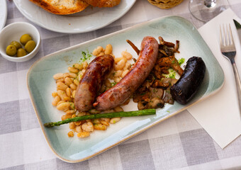 Authentic Catalan platter featuring assorted grilled sausages with side of fried white beans,...