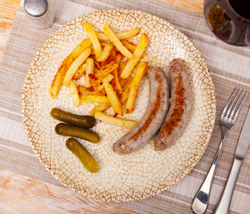 Fried sausages with served with french fries potatoes and marinated cucumbers