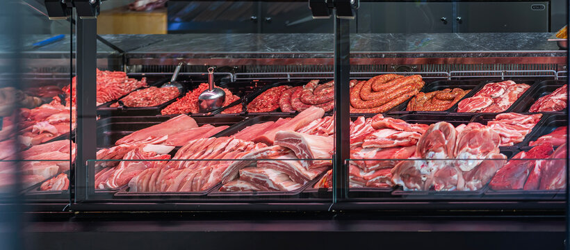 Close-up of meat counter in butcher shop with variety of fresh cuts. Display showcases quality beef, pork, sausages for customers. Fresh meat, beef, minced meat displayed in retail meat counter