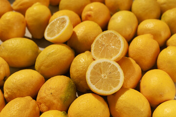 Many lemons spread across a surface, several sliced in half to reveal their fresh, vibrant pulp
