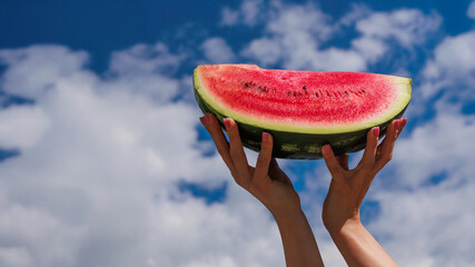 A quarter of a watermelon held in hands with a beautiful sky backdrop