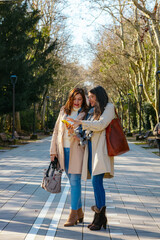 Two mature women using smartphone while walking in a park