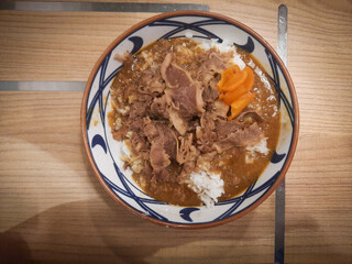 A bowl of Japanese curry rice dish with sliced beef topping served on a wooden patterned table. 