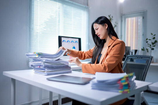A woman is sitting at a desk with a pile of papers in front of her