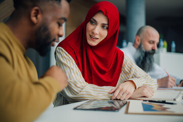 Muslim businesswoman wearing hijab discussing business strategy with african american businessman...