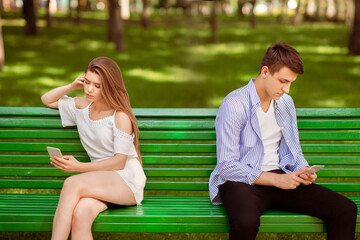 Young girl and her boyfriend with cellphones ignoring each other during dull date at park