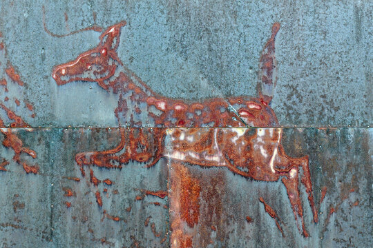 Weathered metal surface with a red-painted deer figure partially obscured by rust and corrosion
