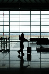 Fototapeta premium young woman against the light at the airport with travel luggage greeting very happily, copy space