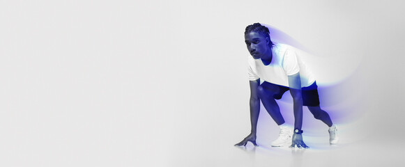 Focused man in athletic wear poised in starting position for sprint, young african american runner guy exuding determination and strength, posing on light grey studio background, copy space