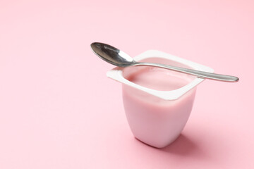 Delicious yogurt in plastic cup with spoon on light pink background, closeup. Space for text