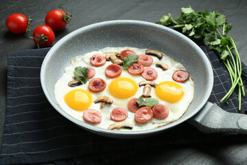 Tasty fried eggs with cut sausages and mushrooms served on black table, closeup