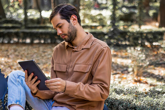 Young man reading e book on tablet in park with bad posture