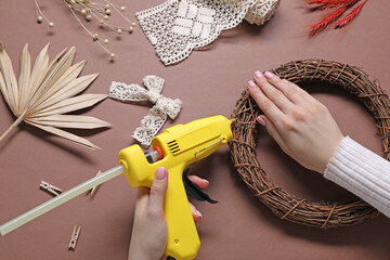 Woman with hot glue gun making craft on brown background, top view