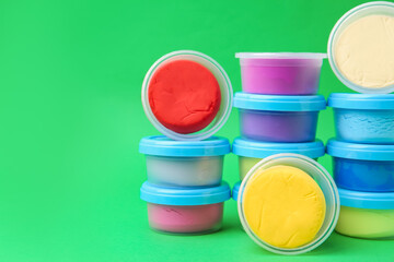Different colorful modeling clay in plastic jars on green background, space for text
