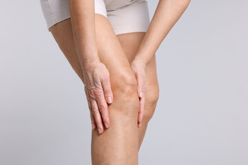 Woman suffering from pain in her knee on light grey background, closeup
