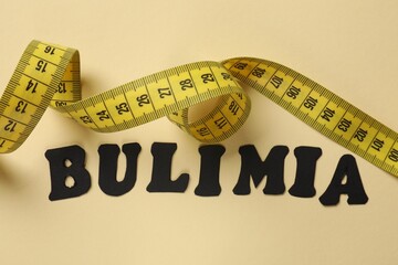 Word Bulimia and measuring tape on beige background, top view