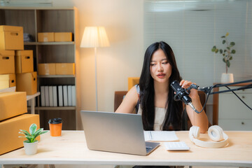 Young asian woman speaking into microphone and recording podcast in home studio, looking at laptop...