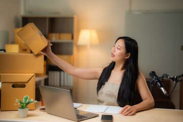 Young Asian entrepreneur presenting products during live selling streaming from a home office,...