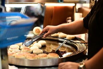 A night market vendor skillfully prepares stuffed pancakes on a hot griddle. The golden-brown crust glistens under the light as steam rises, filling the air with a mouthwatering aroma.