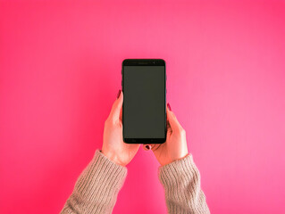 Hands holding black smartphone with blank screen against vibrant pink background, showcasing minimalist mobile technology concept.